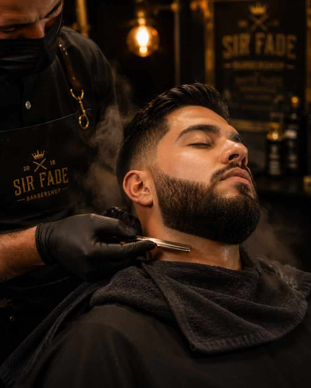 Barbero perfilando con navaja la barba de un hombre en Barbería en El Marqués